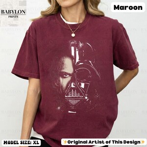 May include: Maroon t-shirt featuring a split image of a person and Darth Vader's helmet. The shirt has the text "BABYLON PRINTS" and "Original Artist of This Design". The model is wearing a size XL.