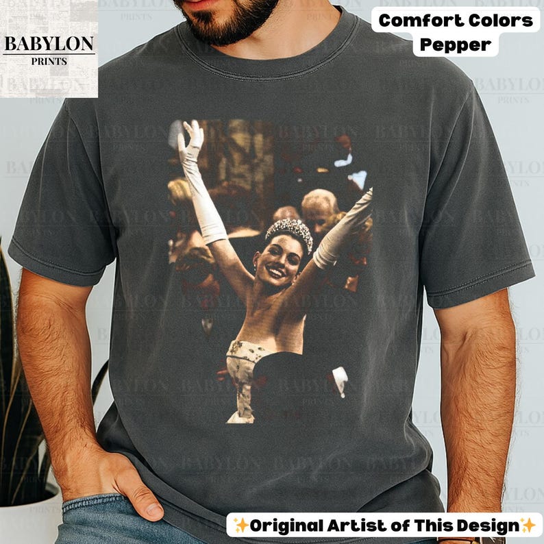 May include: Dark grey Comfort Colors t-shirt with a graphic of a woman wearing a tiara and gloves, arms raised. The text "Comfort Colors Pepper" is above the graphic. The Babylon Prints logo is in the upper left corner.