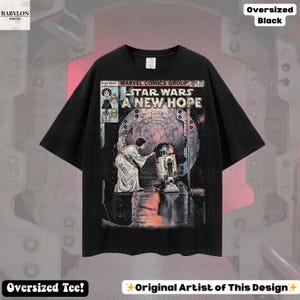 May include: Black oversized t-shirt featuring a comic book-style graphic from Star Wars: A New Hope. The design includes the title, characters, and a scene with R2-D2. The shirt has the text "Oversized Tee!" and "Original Artist of This Design".