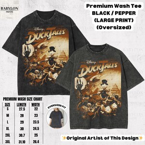 May include: Two black, oversized t-shirts with a distressed finish. Each shirt features a large graphic from Disney's DuckTales, with the show's logo and characters in shades of brown and orange. The shirts have the text "Premium Wash Tee" and a size chart.