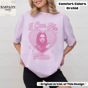 May include: Orchid-colored t-shirt with the text "I Can Fix Him" in a pink heart design. The shirt features a portrait of a man. The words "Comfort Colors" and "Original Artist of This Design" are also visible.