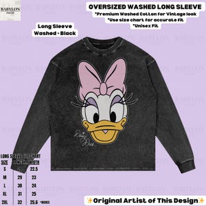 Puede incluir: Camiseta negra de manga larga con un gr&aacute;fico de Daisy Duck. La camiseta presenta un lazo rosa, un pico amarillo y el texto "Daisy Duck". Se incluye la tabla de tallas de la camiseta, con medidas en cent&iacute;metros.