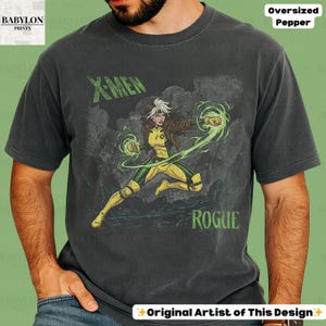 May include: Dark grey t-shirt with a graphic of the X-Men character Rogue. The design includes the text "X-MEN" and "ROGUE" in green. The shirt is labelled "Oversized Pepper" and "Original Artist of This Design."