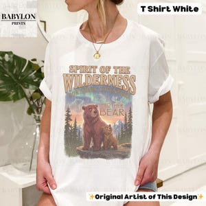 May include: White t-shirt with a graphic of two bears and the text "Spirit of the Wilderness, Northern Adventure, Brother Bear." The design includes a mountain landscape with trees and a colorful sky. The shirt also has the text "Original Artist of This Design."