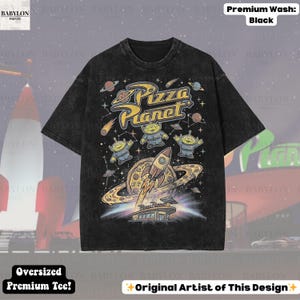 May include: Black oversized premium tee featuring a Pizza Planet graphic. The design includes aliens, a rocket, and a pizza planet logo. The shirt is made of a premium wash fabric.