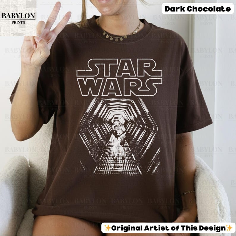 May include: Dark chocolate brown Star Wars t-shirt with a white graphic. The graphic features the Star Wars logo and a detailed image of a hallway with a figure. The shirt is a relaxed fit.