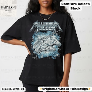 May include: Black t-shirt featuring a Millennium Falcon graphic with blue lightning bolts. The text "Millennium Falcon" is displayed above the spaceship design. The shirt is a comfort color and the model is wearing size XL.