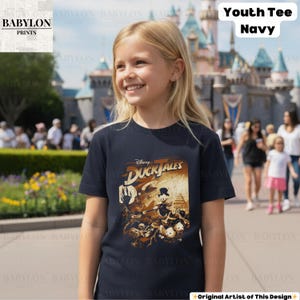 May include: A navy blue youth tee featuring a graphic from Disney's DuckTales. The design includes characters like Scrooge McDuck and Huey, Dewey, and Louie. The shirt also has the text "Youth Tee Navy".