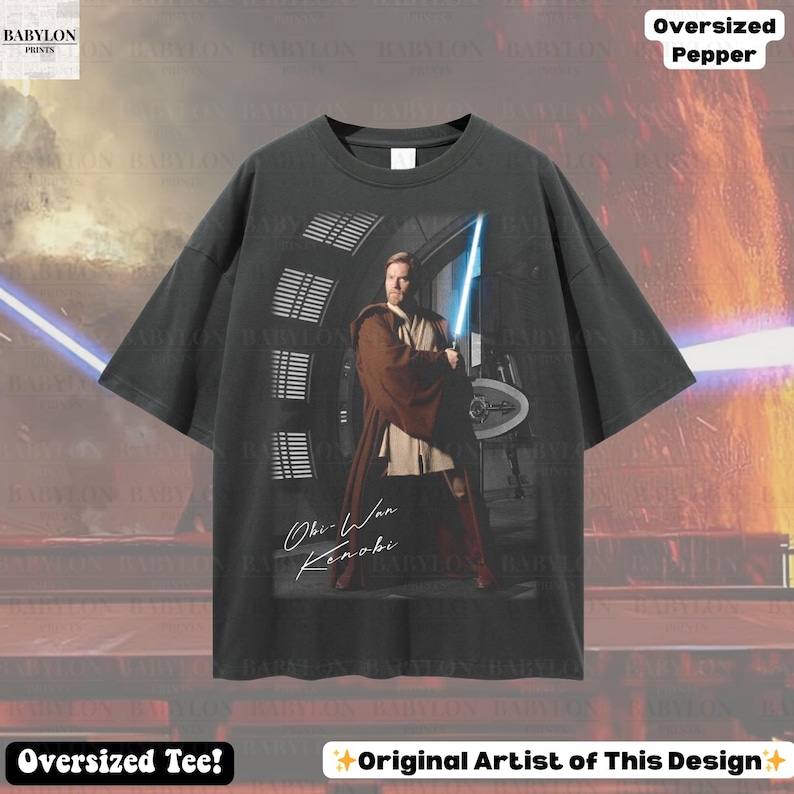 Może przedstawiać: Ciemnoszara koszulka oversize z grafiką Obi-Wana Kenobiego trzymającego niebieski miecz świetlny. Koszulka zawiera tekst "Obi-Wan Kenobi" i "Oversized Tee!"