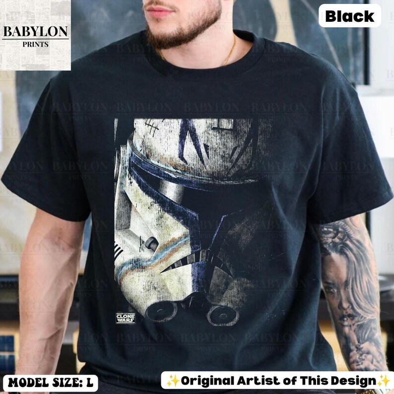 May include: A black short-sleeve t-shirt featuring a large graphic print of a weathered white and blue clone trooper helmet. The design includes distressed textures and the text Babylon Prints in the top left corner and bottom left corner.