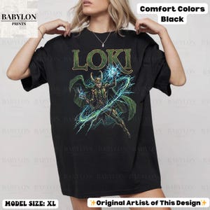May include: Black t-shirt featuring the word "LOKI" in green and a graphic of a character with green cape and blue energy. The shirt is from Babylon Prints and is a Comfort Colors XL.