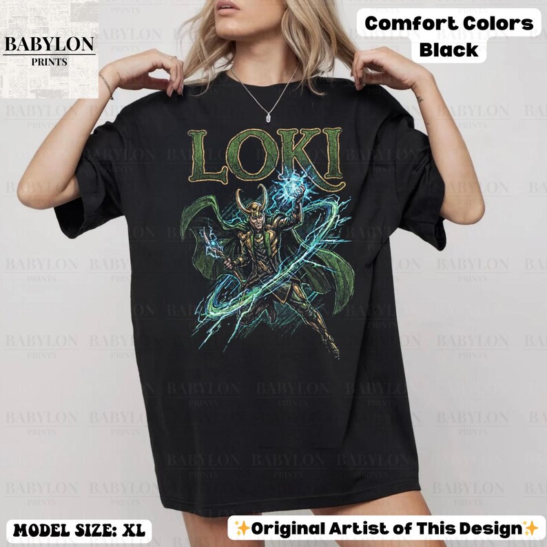 May include: Black t-shirt featuring the word "LOKI" in green and a graphic of a character with green cape and blue energy. The shirt is from Babylon Prints and is a Comfort Colors XL.