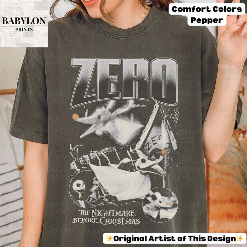 May include: Dark gray t-shirt featuring a graphic from "The Nightmare Before Christmas." The design includes the word "ZERO" in large letters, along with images of Zero and other characters. The text "THE NIGHTMARE BEFORE CHRISTMAS" is also visible.