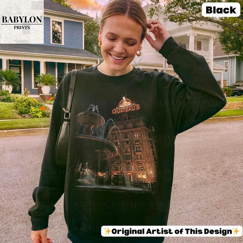 May include: Black sweatshirt with a graphic of a fountain and building, and the text "GUSTEAU'S". The sweatshirt has long sleeves and a crew neck. The text "Original Artist of This Design" is at the bottom.
