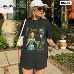 May include: Black t-shirt featuring a graphic from the Disney movie Sleeping Beauty. The design includes Princess Aurora and Maleficent, with the words "Sleeping Beauty" in a vintage font. The shirt is a classic crew neck.