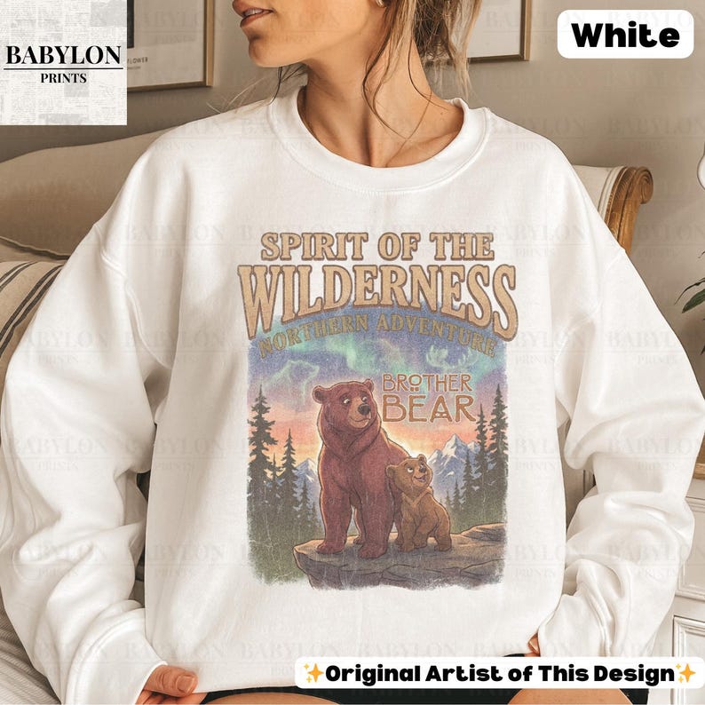 May include: White crew neck sweatshirt with a graphic of two bears and the text "Spirit of the Wilderness" and "Brother Bear." The design includes a mountain and forest scene with a colourful sky.