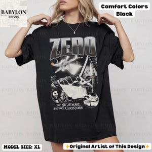 May include: Black t-shirt featuring a graphic design with the word "ZERO" and characters from "The Nightmare Before Christmas." The shirt is labeled "Comfort Colors" and "Original Artist of This Design."
