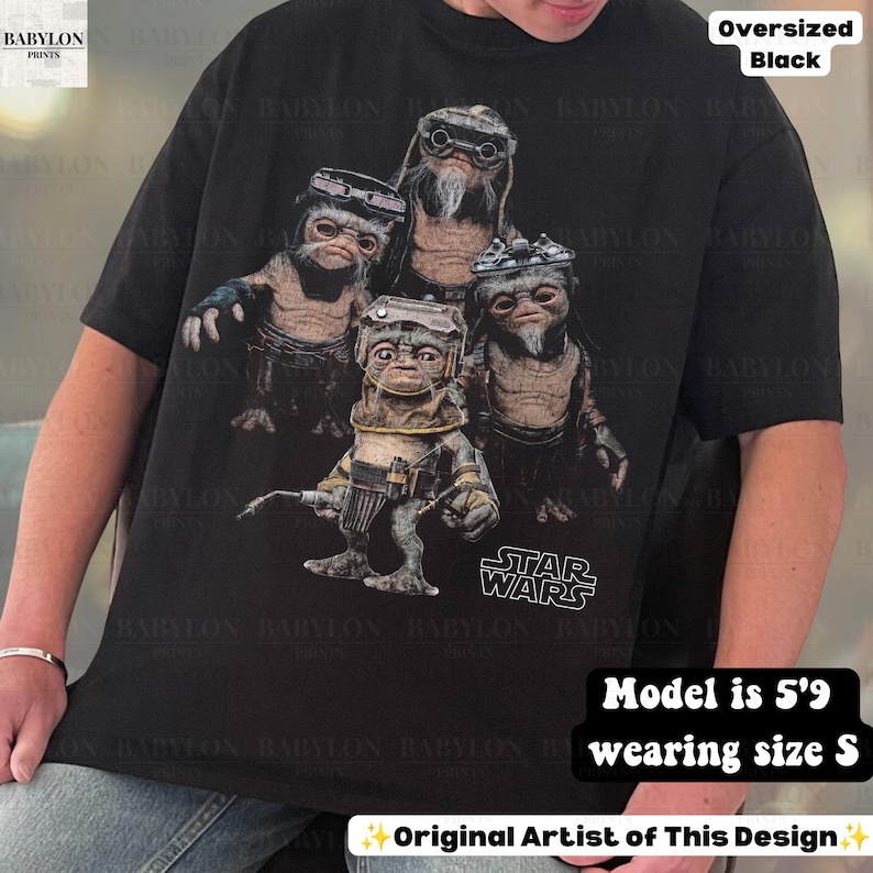 May include: An oversized black t-shirt featuring a graphic print of four Star Wars Ewok characters wearing goggles and gear. The design includes the Star Wars logo in white text at the bottom right. The shirt has short sleeves and a crew neckline.