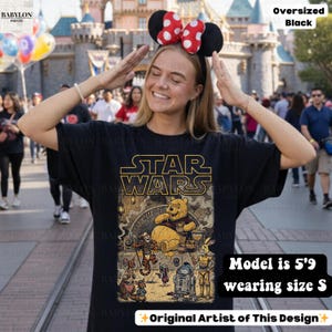 Może przedstawiać: Czarny, obszerny t-shirt z grafiką Star Wars i Kubusia Puchatka. Projekt zawiera napis "STAR WARS" złotymi literami i r&oacute;żne postacie. Modelka ma 1,75 m wzrostu i nosi rozmiar S.