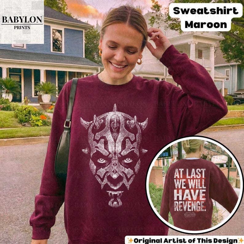 Op de afbeelding: Bordeaux sweatshirt met een witte afbeelding van een gezicht. De achterkant van de sweatshirt heeft de tekst "AT LAST WE WILL HAVE REVENGE." Het Babylon Prints-logo staat in de linkerbovenhoek.