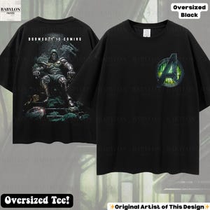May include: Black oversized tee shirt featuring a graphic of a character on a throne with the text "DOOMSDAY IS COMING" on the back. The front of the shirt displays the Avengers logo. The shirt is labeled "Oversized Tee!" and "Original Artist of This Design".