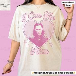 K&ouml;nnte beinhalten: &Uuml;bergro&szlig;es sandfarbenes T-Shirt mit rosa Grafik. Die Grafik zeigt ein herzf&ouml;rmiges Design mit dem Text "I Can Fix Him" und einem Portr&auml;t eines Mannes. Das Shirt hat auch den Text "Original Artist of This Design".