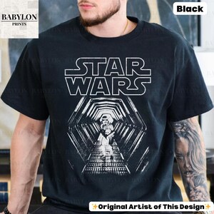 May include: Black t-shirt featuring the Star Wars logo in white block letters above a detailed graphic of a Stormtrooper in a hexagonal tunnel. The shirt is a classic crew neck style.