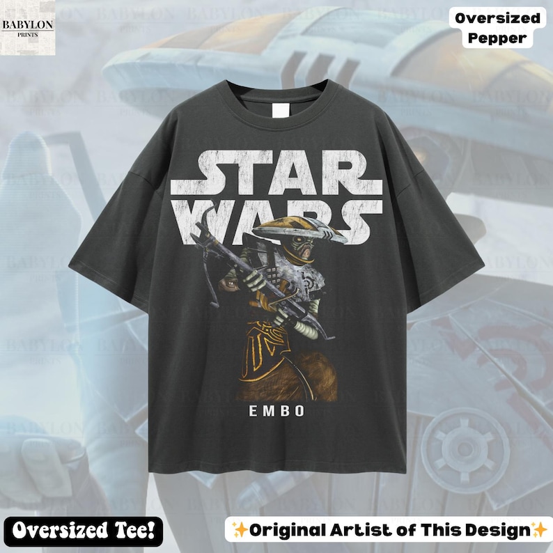 Puede incluir: Camiseta gris oscuro de gran tama&ntilde;o con el logotipo de Star Wars y una ilustraci&oacute;n del personaje Embo. El gr&aacute;fico es blanco, dorado y marr&oacute;n. El texto "EMBO" est&aacute; debajo del personaje. La camiseta tiene el texto "Oversized Tee!" y "Original Artist of This Design".