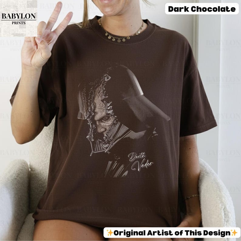 K&ouml;nnte beinhalten: Dunkel schokoladenbraunes T-Shirt mit einer schwarz-wei&szlig;en Illustration von Darth Vader. Der Text "Darth Vader" ist in kursiver Schrift unter dem Bild geschrieben. Das Babylon Prints-Logo ist in der oberen linken Ecke sichtbar.