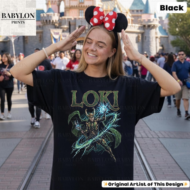 May include: Black t-shirt featuring the word "LOKI" in green, with a graphic of a character in green and gold. The shirt has a crew neck and short sleeves. The text "Original Artist of This Design" is at the bottom.