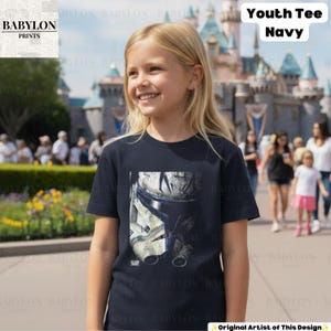 May include: A navy blue short-sleeved t-shirt featuring a graphic print of a weathered white and blue clone trooper helmet on the front. The shirt has a crew neckline and a straight hem, made of a solid-colored fabric with a screen-printed design.