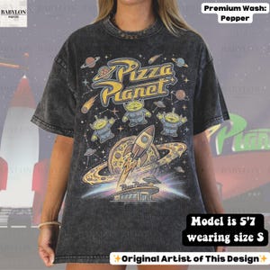 May include: Pepper-washed, oversized t-shirt featuring a colorful Pizza Planet graphic. The design includes the Pizza Planet logo, aliens, a rocket ship, and a pizza planet. The shirt is a size S and the model is 5'7.
