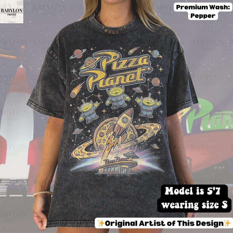 May include: Pepper-washed, oversized t-shirt featuring a colorful Pizza Planet graphic. The design includes the Pizza Planet logo, aliens, a rocket ship, and a pizza planet. The shirt is a size S and the model is 5'7.