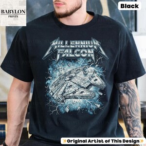 May include: Black t-shirt featuring a graphic of the Millennium Falcon spaceship with the text "Millennium Falcon" in a metal band style font. The design includes blue lightning and the text "Original Artist of This Design."