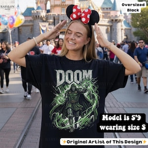 May include: Black oversized t-shirt featuring the word "DOOM" in a distressed font, with a green and black graphic of a character. The text "Original Artist of This Design" is also visible. The model is 5'9" and wearing a size S.