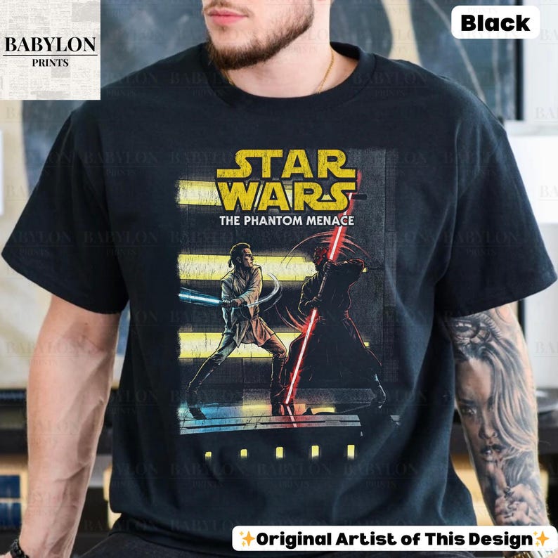 Puede incluir: Camiseta negra con un gr&aacute;fico de Star Wars de "La Amenaza Fantasma". El dise&ntilde;o incluye el logotipo de Star Wars e ilustraciones de personajes con sables de luz. La camiseta tambi&eacute;n tiene el texto "Original Artist of This Design."