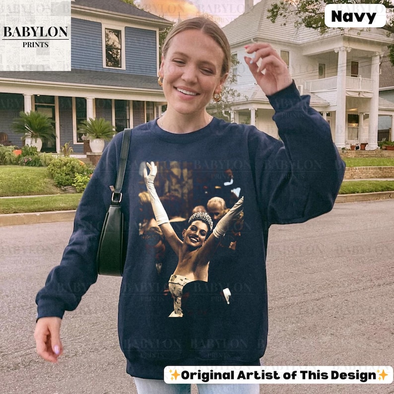 May include: Navy blue sweatshirt with a vintage image of a woman with her arms raised. The sweatshirt has the text "BABYLON PRINTS" on the upper left. The words "Original Artist of This Design" are at the bottom.
