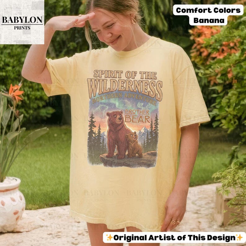 May include: A pale yellow t-shirt with a graphic of two bears and the words "Spirit of the Wilderness." The shirt also has the text "Brother Bear" and "Northern Adventure." The shirt is labeled "Comfort Colors Banana."