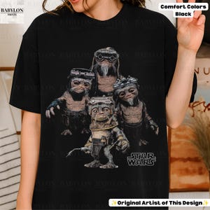 Op de afbeelding: Een zwart t-shirt met korte mouwen en een grafische print van vier kleine, gerimpelde, bruinhuidige wezens die een veiligheidsbril en mechanische uitrusting dragen. Het Star Wars-logo staat in het wit rechtsonder in het grafische ontwerp.