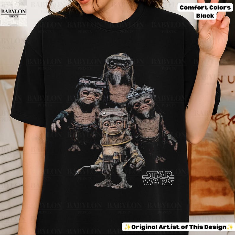 Op de afbeelding: Een zwart t-shirt met korte mouwen en een grafische print van vier kleine, gerimpelde, bruinhuidige wezens die een veiligheidsbril en mechanische uitrusting dragen. Het Star Wars-logo staat in het wit rechtsonder in het grafische ontwerp.