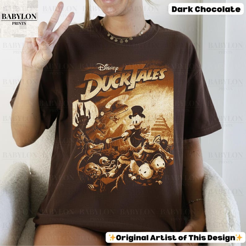 May include: Dark chocolate-colored t-shirt featuring a vintage-style graphic from Disney's DuckTales. The design includes characters like Scrooge McDuck and Huey, Dewey, and Louie, with the text "DuckTales" in a stylized font. The shirt is a relaxed fit.