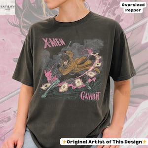 May include: Dark gray oversized t-shirt featuring a graphic of the X-Men character Gambit. The design includes the text "X-MEN" and "GAMBIT" in pink, along with an illustration of the character. The shirt is a Pepper color.