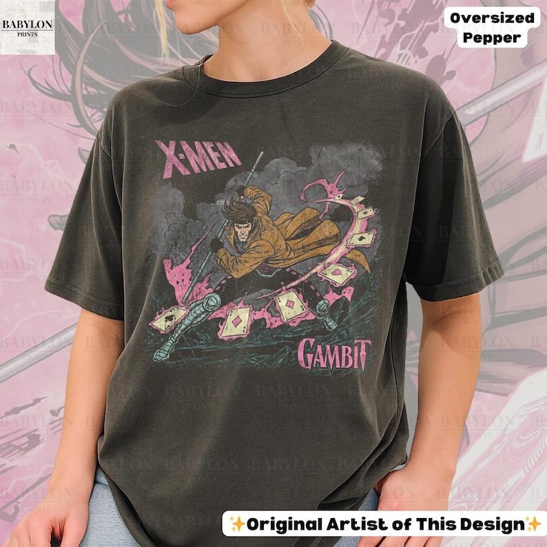 May include: Dark gray oversized t-shirt featuring a graphic of the X-Men character Gambit. The design includes the text "X-MEN" and "GAMBIT" in pink, along with an illustration of the character. The shirt is a Pepper color.