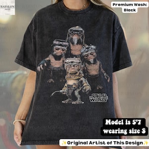 May include: A black acid-wash t-shirt featuring a graphic print of four Ewok characters from Star Wars. The design includes the Star Wars logo in white text. The shirt has a crew neckline and short sleeves, showcasing a vintage-inspired aesthetic.