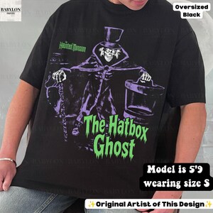 Puede incluir: Una camiseta negra de corte oversize con un gr&aacute;fico de The Hatbox Ghost de The Haunted Mansion. El dise&ntilde;o muestra al personaje con sombrero de copa, sosteniendo un bast&oacute;n y una sombrerera, con el texto The Haunted Mansion y The Hatbox Ghost en verde.