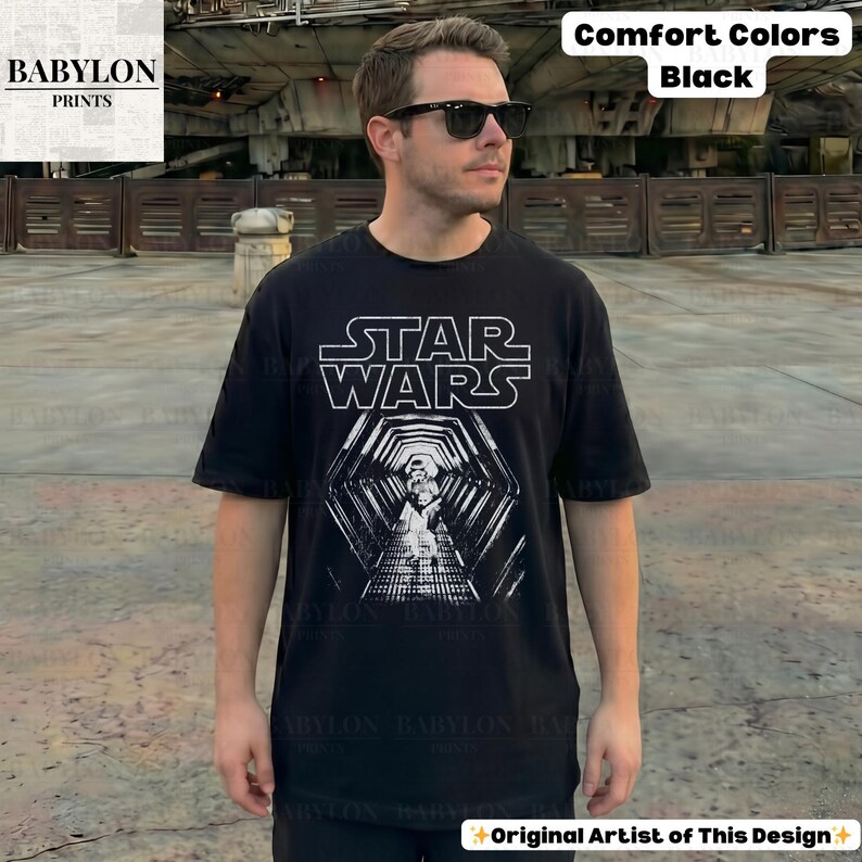 May include: Black t-shirt with the Star Wars logo and a graphic of a Stormtrooper in a tunnel. The shirt is labeled "Comfort Colors" and "Black". The design is by the original artist.