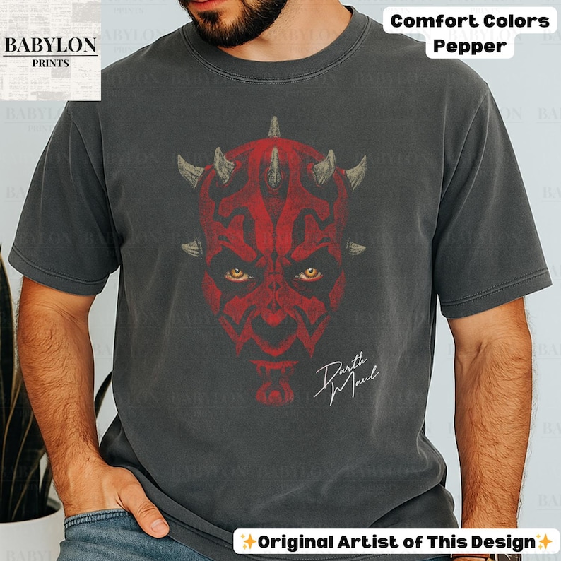 Może przedstawiać: Ciemnoszara koszulka z czerwonym nadrukiem Darth Maul, ż&oacute;łtymi oczami i napisem "Darth Maul". Koszulka jest oznaczona jako "Comfort Colors Pepper" i "Original Artist of This Design".