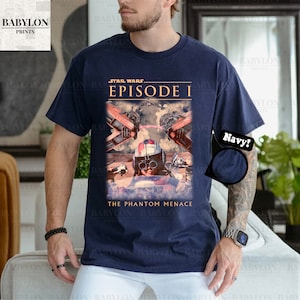 Op de afbeelding: Marineblauw t-shirt met een Star Wars Episode I afbeelding. Het ontwerp bevat beelden uit The Phantom Menace, met een piloot in een helm en ruimtevoertuigen. Het shirt heeft een ronde hals en korte mouwen.