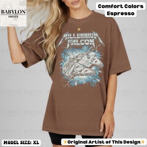 May include: Espresso-colored t-shirt featuring a graphic of the Millennium Falcon with the text "Millennium Falcon" in a stylized font. The shirt is part of the Comfort Colors collection and is a size XL.