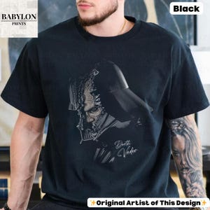 K&ouml;nnte beinhalten: Schwarzes T-Shirt mit einer detaillierten Graustufen-Illustration von Darth Vader. Das Design enth&auml;lt den Text "Darth Vader" in einer stilisierten Schrift. Das Shirt hat auch den Text "Original Artist of This Design".